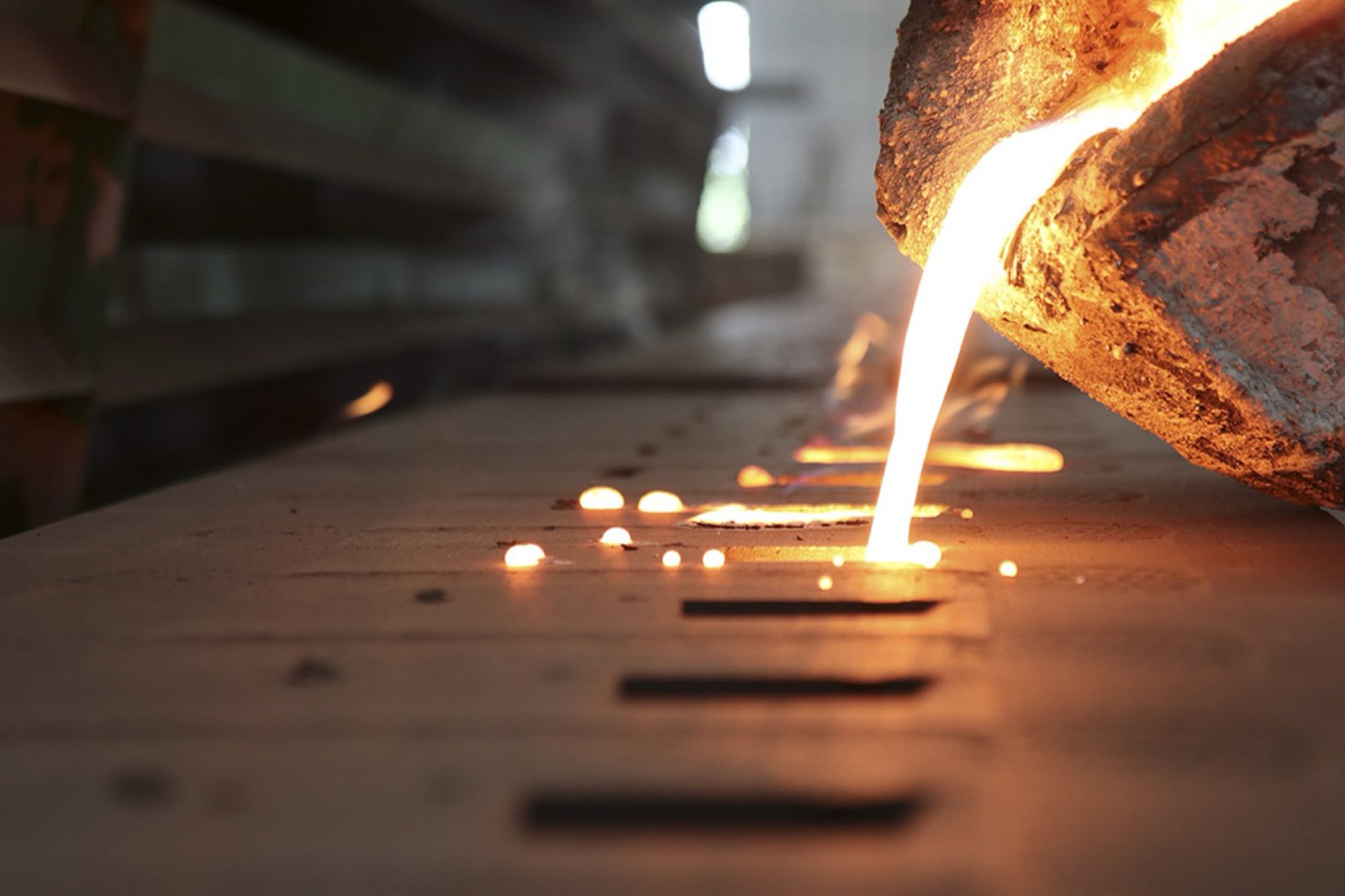 Molten metal poured from a ladle along a line of sand molds