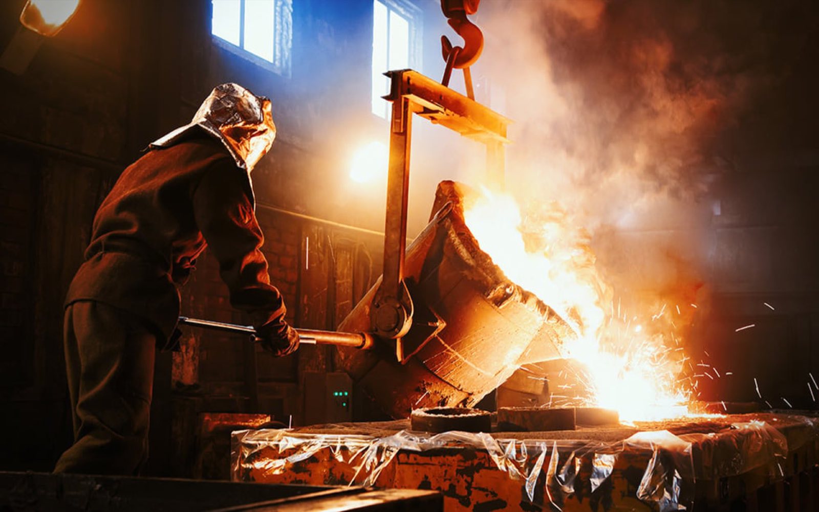 A foundry worker guiding a ladle of molten metal over a mold