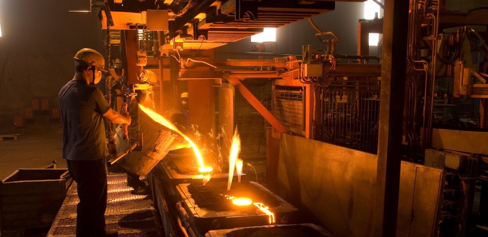 A foundry worker pouring molten iron into a mold on the line
